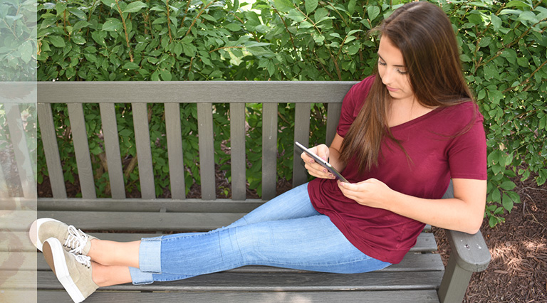 Teen girl sitting on a bench using tablet